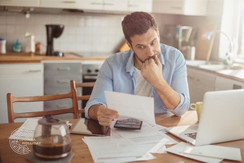 Man sitting in front of laptop, holding a bill with financial problems