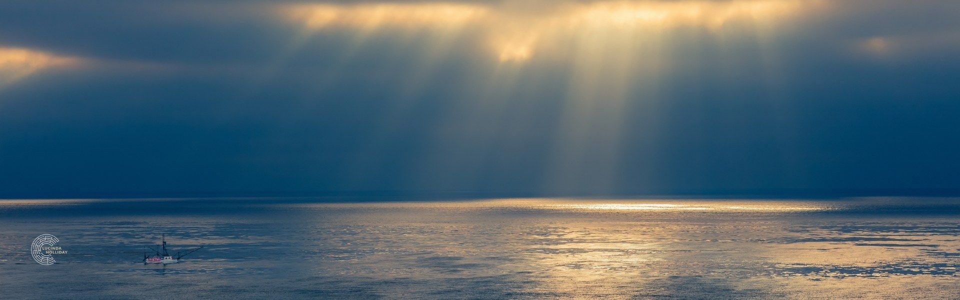 Sun breaking through clouds onto a calm sea with boat