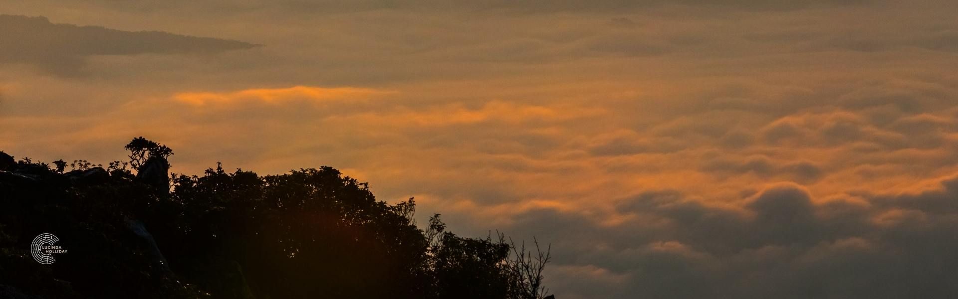 Sunlight shining through dark clouds View over mountains above the clouds to sunset