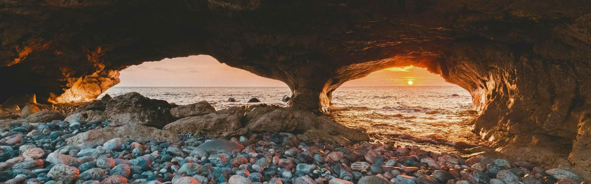 Sunset through natural arch on rocky beach